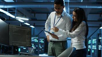 Team of programmers in high tech data center troubleshooting issues using tablet. Teamworking colleagues in server farm using device, establishing performance benchmarks, camera A photo