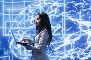 Programmer uses laptop to analyze AI models with large digital brain displayed behind. IT professional holding notebook, using machine learning to better understand and develop artificial intelligence photo