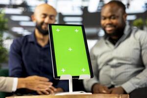 Focus on green screen tablet used by colleagues in blurry background preparing for business meeting. Close up of mockup device used by people doing research analysis for startup organization photo