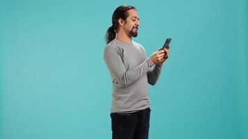 Happy man texting best friend using smartphone, reading messages. Relaxed person having fun while chatting with mate on mobile phone, isolated over blue studio background, camera A photo