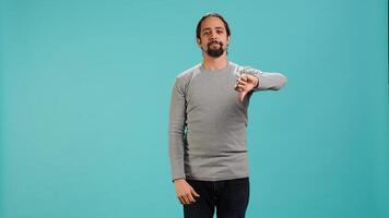 Upset man showing thumbs down sign gesturing, being disapproving. Disappointed Arab person against gaming, doing rejection hand gesture, isolated over studio background, camera A photo