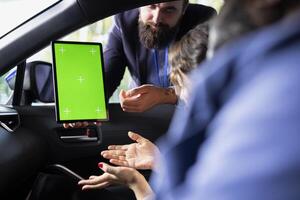 Salesperson using green screen tablet during test drive, negotiating price and car features with clients. Showroom employee persuading hesitant customers to buy vehicle using mockup device photo