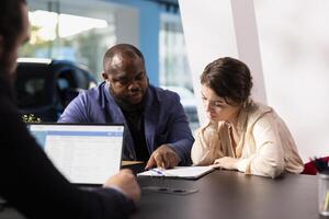 Customers in showroom completing credit application and financing paperwork after deciding to purchase new car. Salesman in dealership discussing financing options with clients photo