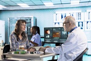 Senior doctor and patient discussing diagnostic results in a modern medical office, showcasing advanced technology using a computer displaying x rays and MRI scans. Care management. photo