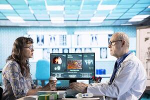 Senior doctor and patient discussing diagnostic results in a modern medical office, showcasing advanced technology using a computer displaying x rays and MRI scans. Care management. photo
