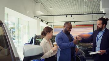 Car dealership salesman completing purchase paperwork and documentation after agreeing terms with customers. Agent giving sale contract for clients to sign after offering vehicle keys, camera B photo