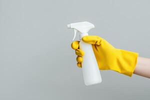 Hand in Yellow Glove Holding a White Spray Bottle Against Grey Background photo
