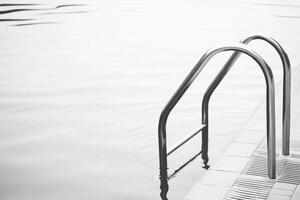 Minimalist Poolside Scene with Silver Ladder and Tranquil Water Surface photo