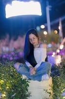 Young Woman Sitting on Barrel Surrounded by Colorful Lights at Night photo