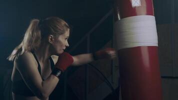 Strong woman fighter practicing fast and strong hand strikes on a punching bag in an abandoned room video