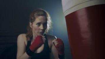 Woman fighter practicing throwing fast, hard punches on a punching bag, practicing at home, in the garage. Slow motion, 4k video