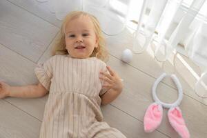 Child lying on the floor with bunny ears and colorful eggs during a playful holiday celebration photo