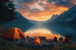 Camping tent and burning campfire by the lake at sunset with mountain background. photo