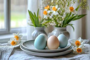 Easter eggs are laying on plates near daffodils and lilies of the valley in window photo
