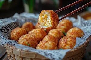 Chopsticks holding arancini rice ball with melted cheese and corn filling. photo