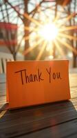Thank you card placed on a wooden table with sunlight shining through trees at sunset photo