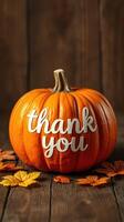 Bright orange pumpkin with thankful message and autumn leaves on rustic wooden table photo