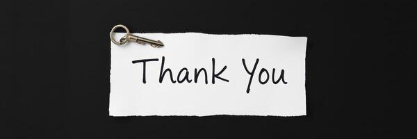 Expressing gratitude with a handwritten note attached to a key on a dark surface photo