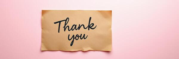 Gratitude expressed through a handwritten note on brown paper set against a soft pink background photo