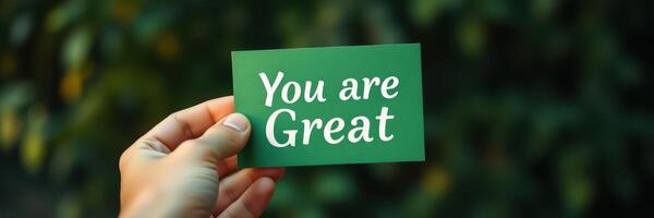 Hand holding card with motivational message in nature setting during daylight photo