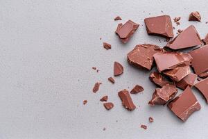 Broken pieces of dark chocolate on a gray background photo