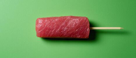 Raw tuna steak on a stick, close up view against a green background photo