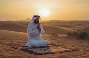 Arabic man praying in the desert at sunset photo