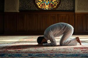 A man in white is kneeling on the floor in a mosque photo