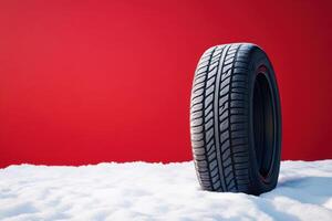 Tire resting on snow against a bold red backdrop showcasing winter readiness and performance photo