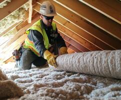 Worker installing insulation in residential attic during daylight hours for improved energy efficiency photo