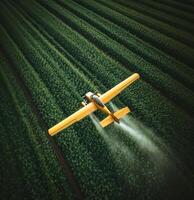Crop-dusting aircraft sprays fertilizers over lush green fields in broad daylight photo