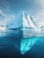 Massive iceberg floating in calm waters reflects its stunning shape under a bright blue sky photo