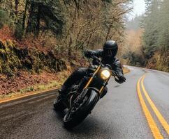 Motorcycle rider navigates a winding road through a lush forest on a rainy day photo