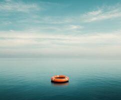 Bright orange lifebuoy floats gently on calm waters under a vast blue sky at dusk photo