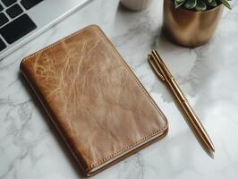 Pen lying on leather notebook with smartphone on marble desk photo
