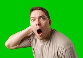 A surprised man stands in front of a bright green screen, expressing shock with his mouth open photo
