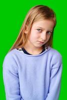A young child in a light purple sweater gazes against a green background while deep in thought photo