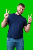 Man smiling and giving peace signs while standing against a bright green backdrop photo