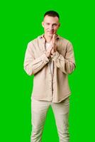 Young Man Wearing Beige Jacket and Pants Standing With Hands Together Against Bright Green Background photo