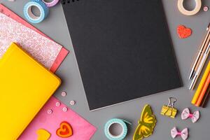 Crafting supplies arranged on a gray surface with a blank notebook, scissors, washi tape, and colorful embellishments photo