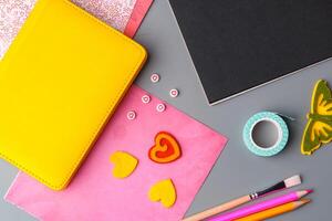 Crafting supplies arranged on a gray surface with a blank notebook, scissors, washi tape, and colorful embellishments photo