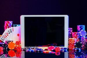 A gaming tablet surrounded by colorful poker chips at a casino table during a night gambling session photo