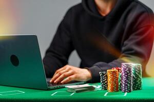 A player engages with online poker on a laptop, surrounded by colorful chips and playing cards on a green table photo
