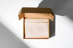 A small, empty cardboard box with unwrapped parchment resting inside on a bright, sunlit table photo