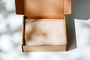 A small, empty cardboard box with unwrapped parchment resting inside on a bright, sunlit table photo