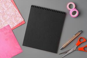 Crafting supplies arranged on a gray surface with a blank notebook, scissors, washi tape, and colorful embellishments photo