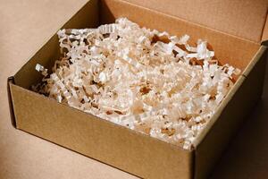 Open cardboard box with shredded paper packaging resting on a light brown surface illuminated by soft natural light photo