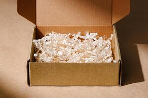 Open cardboard box with shredded paper packaging resting on a light brown surface illuminated by soft natural light photo