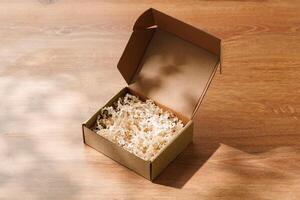 Open cardboard box with shredded paper filling on a wooden table photo