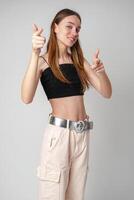 Young Woman in Black Crop Top and Beige Pants Points at the Camera photo